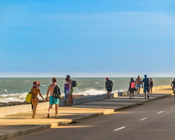 Ludzie spacerują i jeżdżą na rowerach wzdłuż promenady nad oceanem w słoneczny dzień.