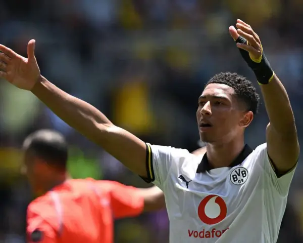 Jude Bellingham, con los brazos en alto, celebra un gol. El joven jugador del Dortmund, con su camiseta blanca, inspira a la afición.