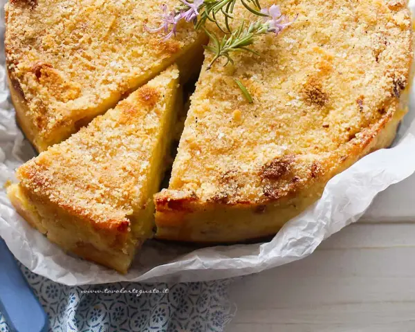 Delizioso gateau di patate dorato e croccante, guarnito con rosmarino fresco. Una fetta è già stata tagliata, invitando ad assaggiarlo.