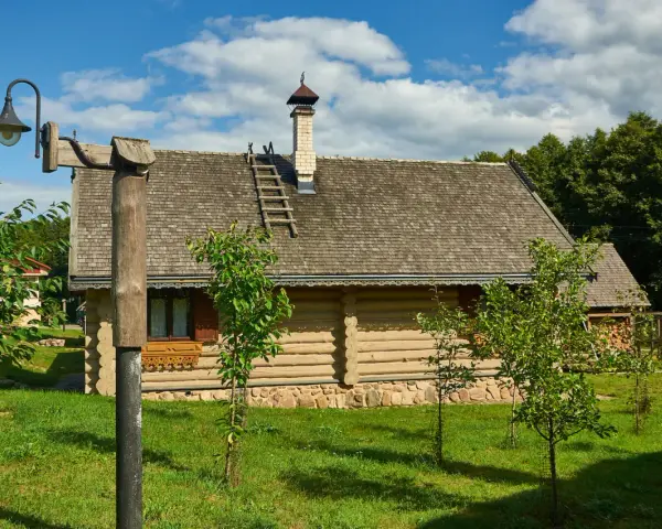 Drewniany dom z kamienną podmurówką i gontowym dachem, otoczony zielenią. To malownicze grunty rolne zabudowane, gdzie tradycja spotyka się z naturą.