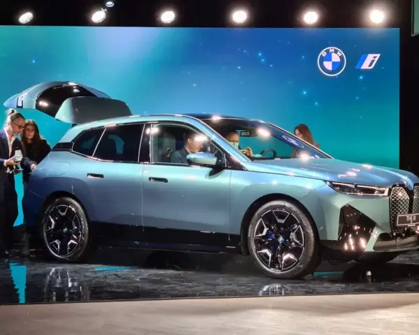 Jasnoniebieski elektryczny SUV BMW iX z otwartą klapą bagażnika na scenie.