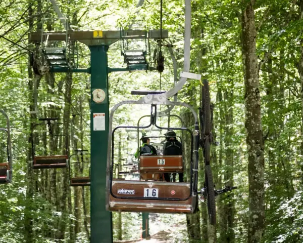 La funivia Monte Amiata trasporta due persone e una mountain bike attraverso un bosco lussureggiante.