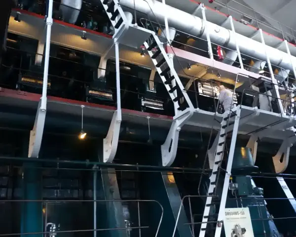 Ogromna, wielocylindrowa jednostka napędowa, prawdopodobnie największy silnik na świecie, z metalowymi schodami i platformami dla obsługi.
