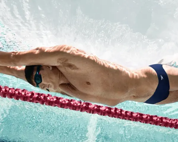Un nageur en plein effort, profitant des bienfaits natation. La lumière joue sur son corps musclé, soulignant la puissance de ses mouvements sous l'eau.