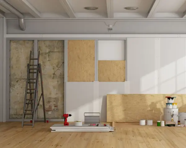 Chantier de rénovation avec panneaux de bois, échelle, outils et pots de peinture.