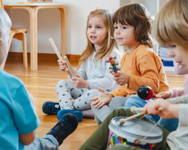 Kinder musizieren mit Holzstäben, Rasseln, einer Trommel und einem Maracas. Welche Instrumente gibt es?