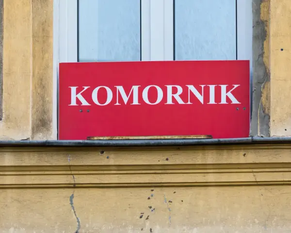 Czerwona tablica z napisem "KOMORNIK" na tle okna. Może to oznaczać zajęcie komornicze wynagrodzenia.