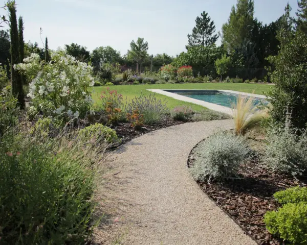 Une allée de jardin originale serpente vers une piscine, bordée de lavande, de fleurs blanches et d'arbustes verts.