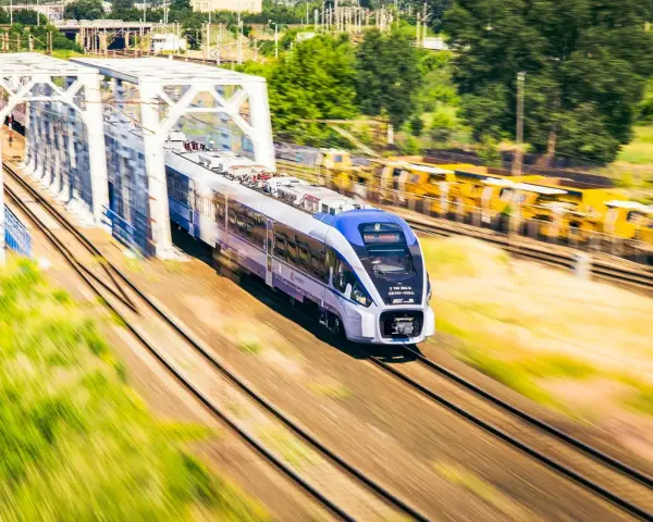 Nowoczesny pociąg PKP Intercity z niebieskim przodem mija biały most kolejowy.