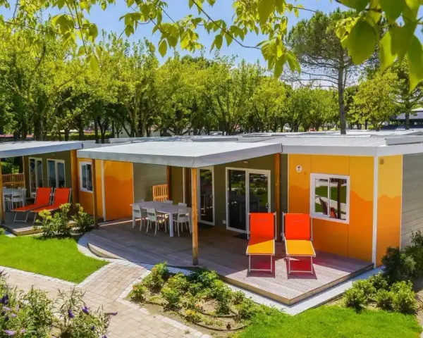 Kolorowe domki na kempingu, z tarasami i leżakami, otoczone zielenią. Prawdziwy camping garden paradiso!