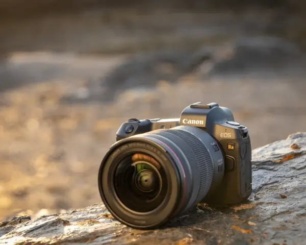 Aparat Canon EOS Ra z obiektywem RF 15-35mm f/2.8L IS USM leży na kamieniu.