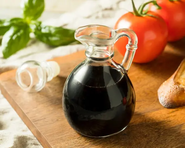 Mały dzbanuszek z ciemnym, gęstym **octem balsamicznym** obok pomidorów, bazylii i grzanek.
