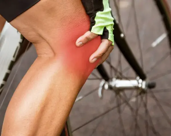 Cyclist holding knee with red pain indicator. Learn about cycling knee pain exercises to get back on the road.