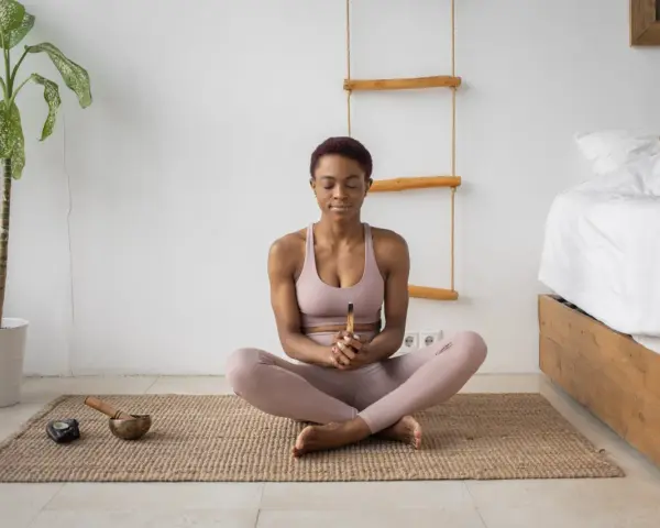 Mujer meditando en postura de loto, con los ojos cerrados y un palo de incienso en las manos. A su lado, un cuenco tibetano y una vela. Aprende como meditar para encontrar la paz interior.