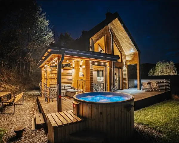 Drewniany domek z jacuzzi i tarasem, idealne miejsce na babia góra noclegi. Oświetlony girlandami, zaprasza do relaksu.
