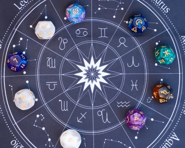Kolorowe kostki z symbolami zodiaku i liczbami, leżące na tle z kołem horoskopowym. Każda liczba w numerologii ma swoje znaczenie.