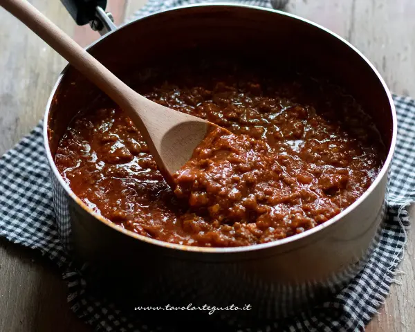 Un pentolino pieno di profumato ragù di carne, pronto per condire la pasta. Un cucchiaio di legno mescola la salsa densa e invitante.