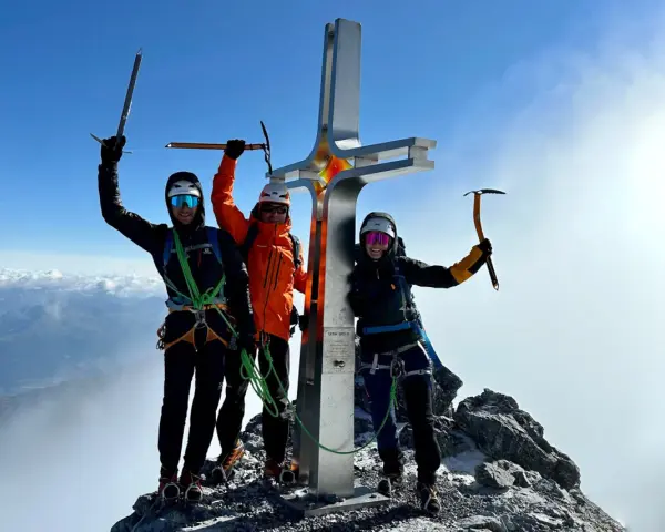 Drei Bergsteiger feiern am Gipfelkreuz des Ortler Normalwegs ihren Erfolg.