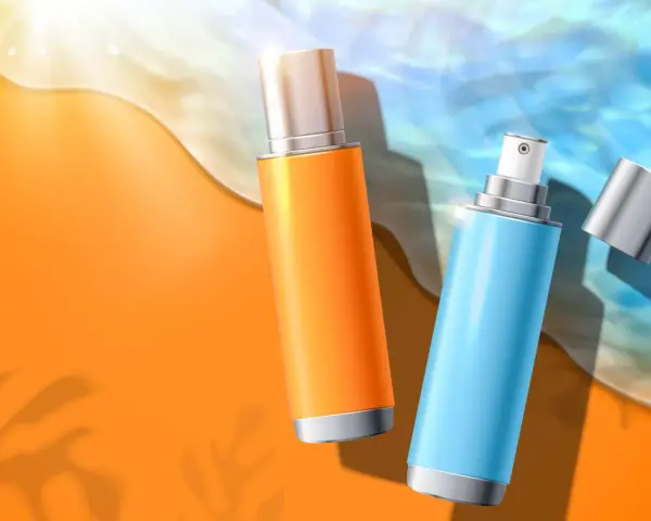 Due flaconi spray, uno arancione e uno azzurro, sulla sabbia dorata con onde marine. Protezione solare con butyl methoxydibenzoylmethane.