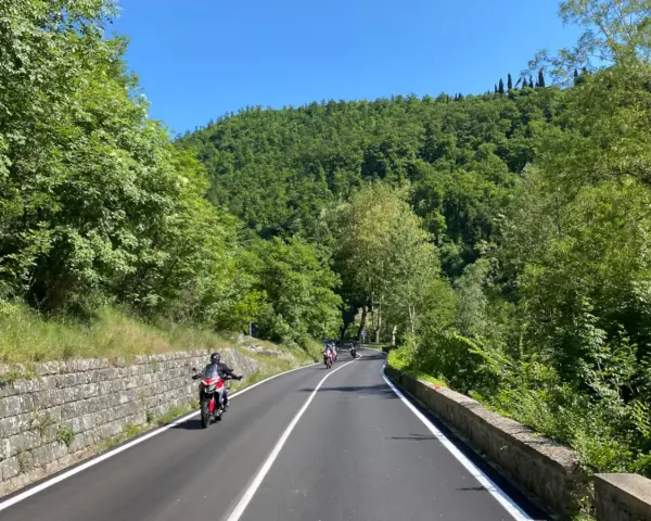 Motociclisti su strade panoramiche in Emilia Romagna, tra colline verdi e cielo azzurro.