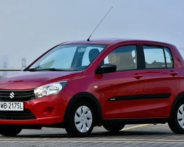 Czerwony Suzuki Celerio z polskimi tablicami rejestracyjnymi WB 2175L zaparkowany na zewnątrz.