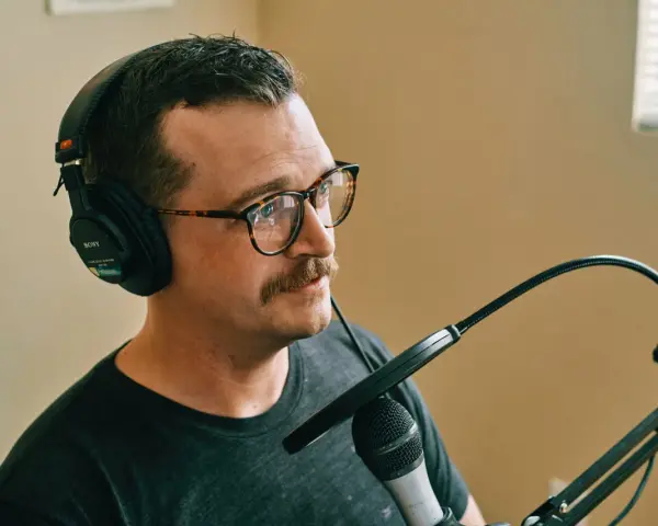 Mężczyzna w okularach i słuchawkach Sony nagrywa podcast. Dba o odpowiedni gain staging, by dźwięk był czysty.