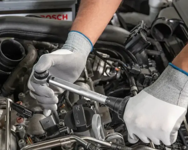 Mechanik w białych rękawiczkach dokonuje wymiany świec zapłonowych w silniku samochodu, używając klucza dynamometrycznego.