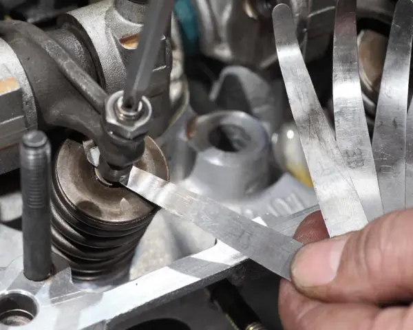 Mechanik sprawdza luzy zaworowe za pomocą szczelinomierza w silniku samochodowym.