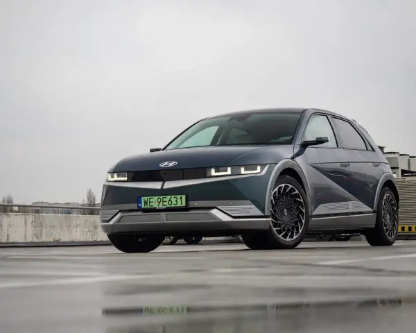 Hyundai Ioniq 5, z charakterystycznymi światłami i felgami, prezentuje swoje imponujące wymiary na mokrym parkingu.