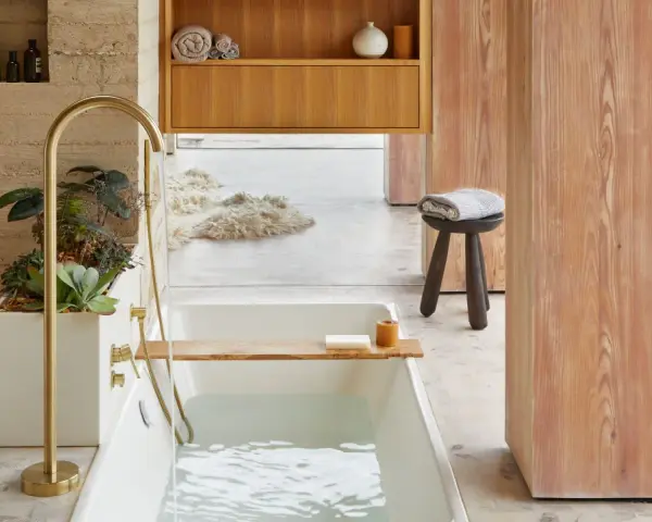 Bain relaxant avec baignoire remplie, robinetterie dorée, plantes et bois. Une belle inspiration salle de bain.