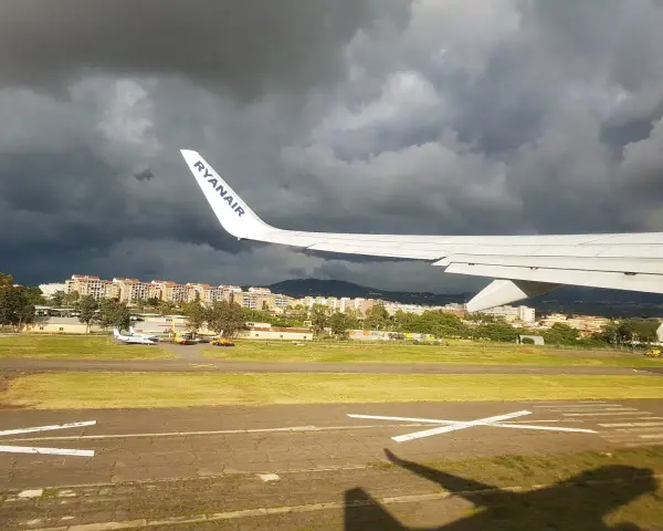 Skrzydło samolotu Ryanair nad lotniskiem, ciemne chmury na niebie.
