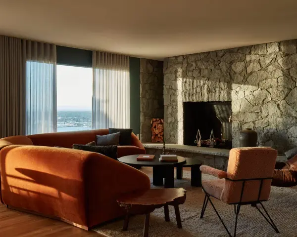 Sofá curvo naranja y chimenea de piedra, con un toque de diseño años 50.