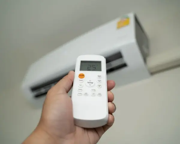 Dłoń trzymająca pilot do klimatyzatora, ustawiająca temperaturę 25°C. Ogrzewanie klimatyzatorem to komfort.