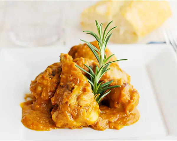 Sabroso pollo con almendras en una salsa dorada, adornado con romero fresco. Un plato que invita a disfrutar.