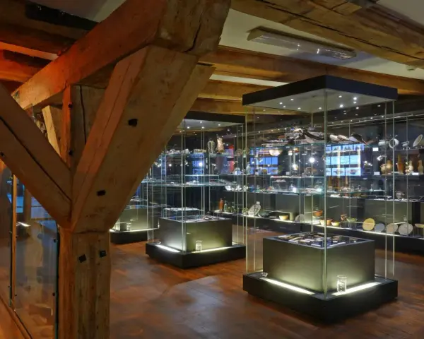 Wnętrze muzeum z zabytkowymi belkami i gablotami pełnymi artefaktów. Wśród nich można odnaleźć spichlerz błękitny baranek, symbol dawnych czasów.