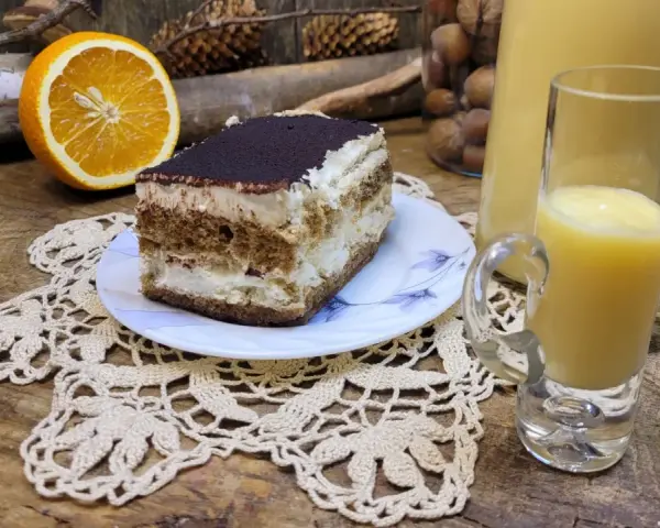Słodki deser tiramisu, połówka pomarańczy i kieliszek likieru ze skórek pomarańczy na drewnianym blacie.