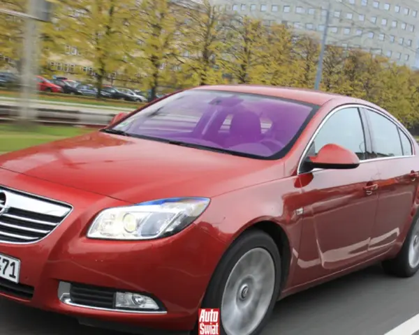 Czerwony Opel Insignia 1.6 Turbo w ruchu ulicznym. Wady tego modelu mogą dotyczyć np. spalania.