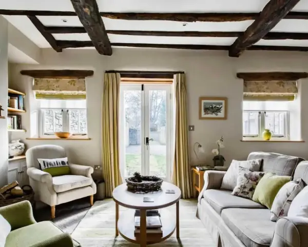 Salon confortable d'un maison cottage anglais, avec poutres apparentes, fauteuils douillets et vue sur le jardin.