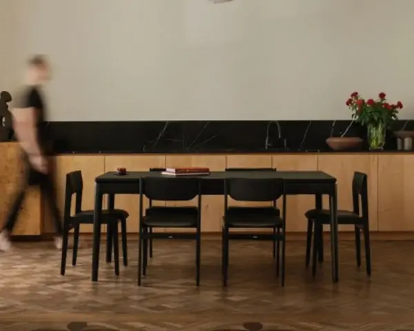 Jadalnia z czarnym stołem i krzesłami, otoczona meblami w ciepłych odcieniach dębu. W tle bukiet czerwonych róż.