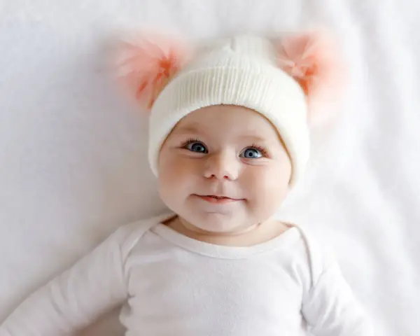 Ein süßes Baby mit blauen Augen und einer Mütze mit Bommeln. Man fragt sich, welche Augenfarbe bekommt mein Kind.