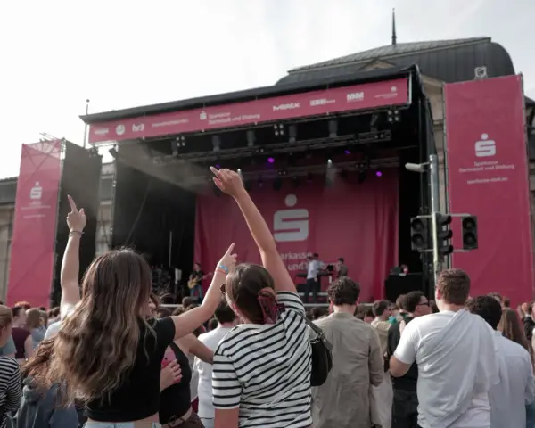 Menschen jubeln bei einem Open-Air-Konzert vor einer Bühne mit Sparkassen-Logo.