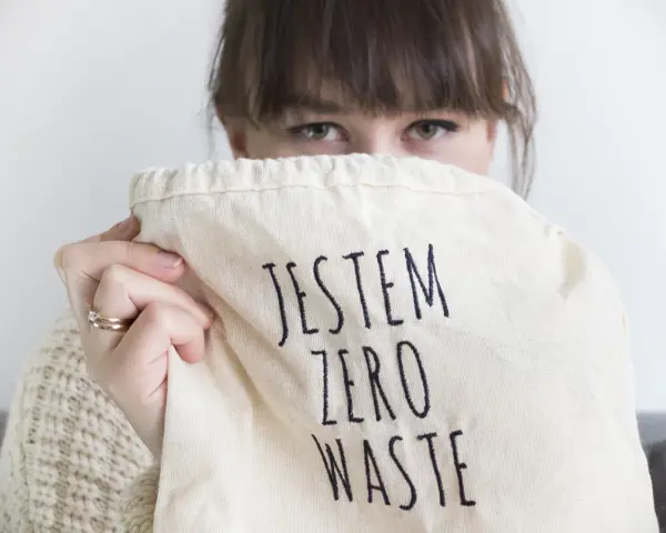 Sylwia Majcher, z uśmiechem ukrytym za torbą z napisem "Jestem Zero Waste", pokazuje swoje zaangażowanie w ekologię.