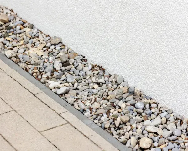 Kiesbett als Spritzschutz am Haus, neben gepflastertem Weg.
