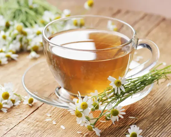 Une tasse de tisane de camomille, idéale pour le rhume traitement, entourée de fleurs fraîches sur un fond en bois.