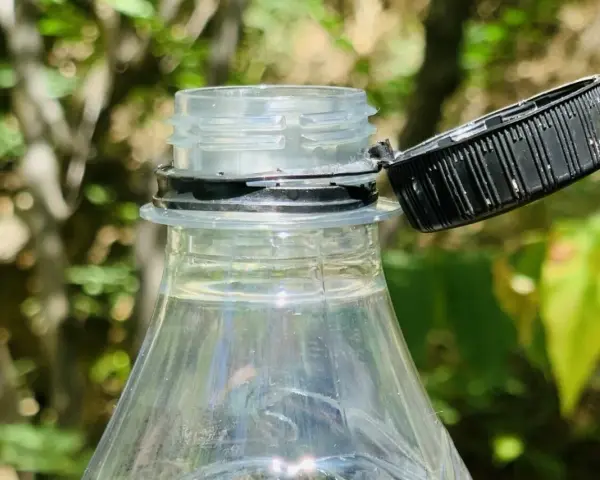 Nakrętki od butelek są przytwierdzone, by zapobiec ich zgubieniu i ułatwić ponowne zakręcenie. Widoczny fragment plastikowej butelki z otwartą, czarną nakrętką.