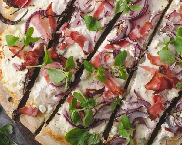 Flammkuchen mit Speck, roten Zwiebeln und frischen Kräutern – tolle Flammkuchen Belag Ideen für jeden Geschmack.