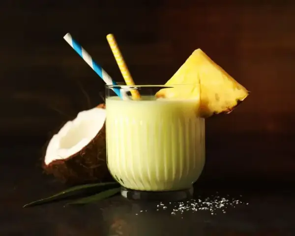 Orzeźwiający drink z mlekiem skondensowanym, ananasem i kokosem, ozdobiony słomkami. Idealny na tropikalne popołudnie.