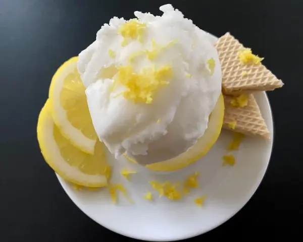 Erfrischendes zitroneneis wie beim Italiener, garniert mit Zitronenschale, Zitronenscheiben und Waffeln auf einem weißen Teller.