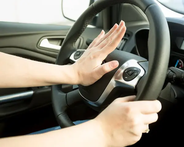 Hand drückt auf Hupe im Auto. Wann darf man hupen? Nur in Notfällen, um einen Unfall zu vermeiden.