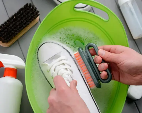Come lavare le Superga bianche: una scarpa immersa in acqua saponata, mentre una mano la strofina con una spazzola.
